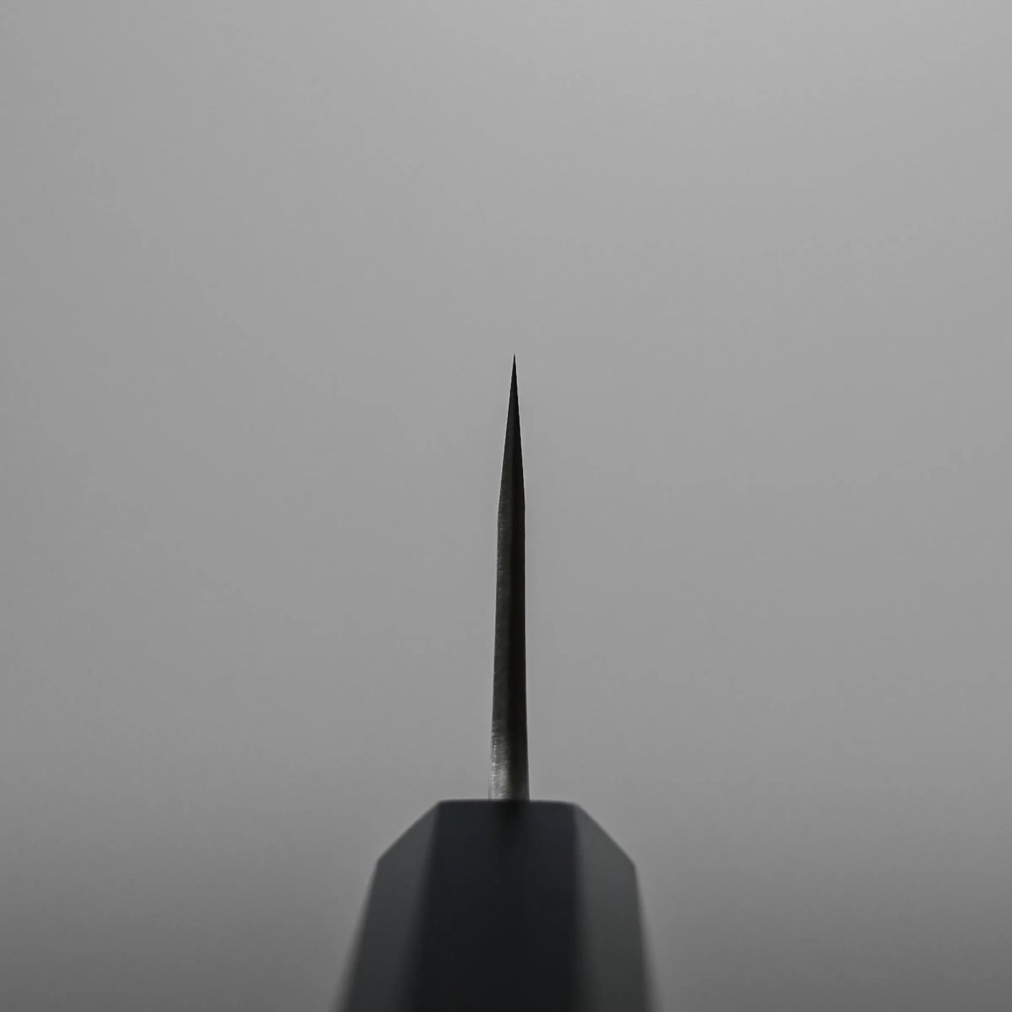 Choil shot of a honesuki knife, a traditional Japanese boning knife, set against a plain, light gray background.