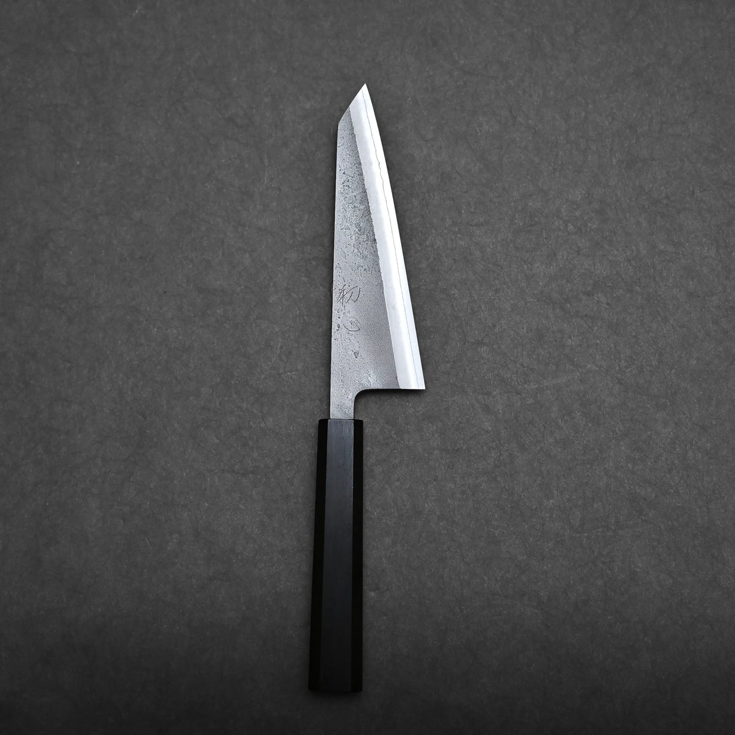 A Japanese-style honesuki knife with a straight-edged blade and a black handle is placed on a dark gray textured surface.