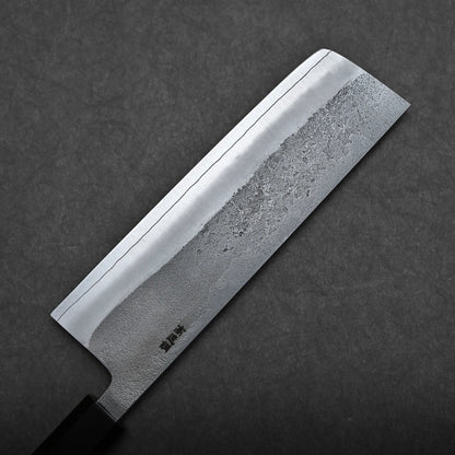 A close-up of a Japanese-style kitchen knife with a rectangular blade on a dark textured surface. The blade has a visible pattern and a straight cutting edge.