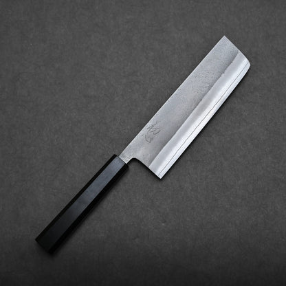 A Hatsukokoro x Yoshikane nashiji SKD nakiri 165mm with a rectangular blade and a black handle is displayed on a dark, textured surface.
