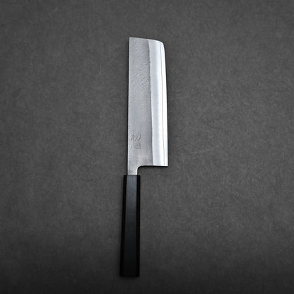 A Japanese-style kitchen knife with a rectangular blade and a black handle is placed on a dark gray textured surface. The blade has a slightly reflective finish and some visible markings near the handle.