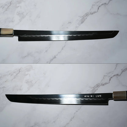 Two views of a Japanese honyaki sakimaru takohiki knife on a marble-patterned surface. The blade is long, narrow, and single-beveled, with a curved tip and visible hamon line. One view shows the edge and temper line; the other shows engraved kanji near the handle.