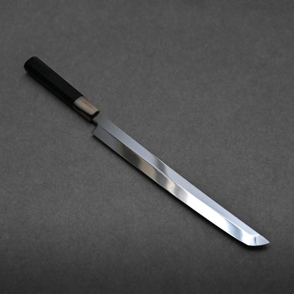 A long, single-edged honyaki sushi knife with a shiny, straight blade and a black handle is displayed on a dark gray surface.
