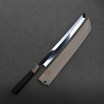 A Yoshikazu Ikeda aogami#1 honyaki sakimaru yanagiba 300mm with a black handle rests next to its wooden sheath on a dark gray surface. The mizuhonyaki aogami#1 sakimaru blade is shiny and straight, tapering to a sharp angled point.