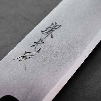 A close-up of a gyuto knife blade with Japanese characters engraved on the metal, shown against a dark, textured background.
