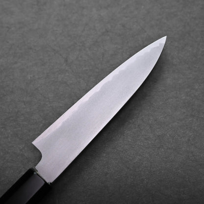 A close-up of a sharp petty knife with a silver blade and a black handle, placed on a dark, textured surface.