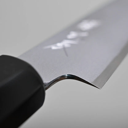 Close-up of the blade and handle of a petty knife, showing the choil finish and Japanese characters engraved on the metal. The background is plain and out of focus.