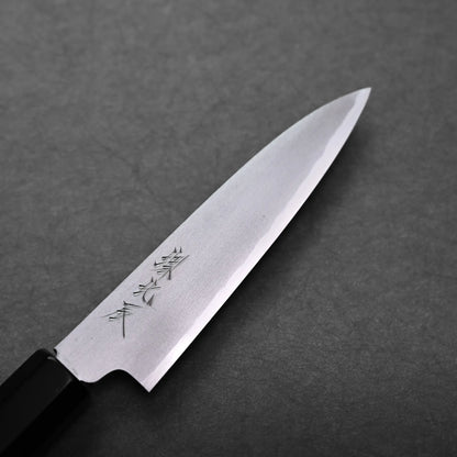A close-up of a Japanese petty knife with a sharp, pointed blade and engraved characters on the metal, placed on a dark textured surface.