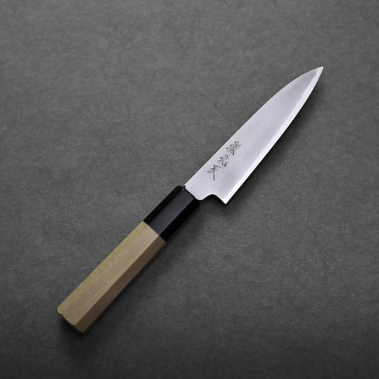 A Yoshikazu Ikeda shirogami#2 petty knife 120mm with a wooden handle and a sharp, pointed stainless steel blade engraved with Japanese characters, placed on a dark textured surface.