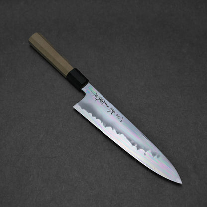 A tall gyuto features a shiny, engraved silver blade with an aogami#1 core and wooden handle, shown on a dark gray surface.