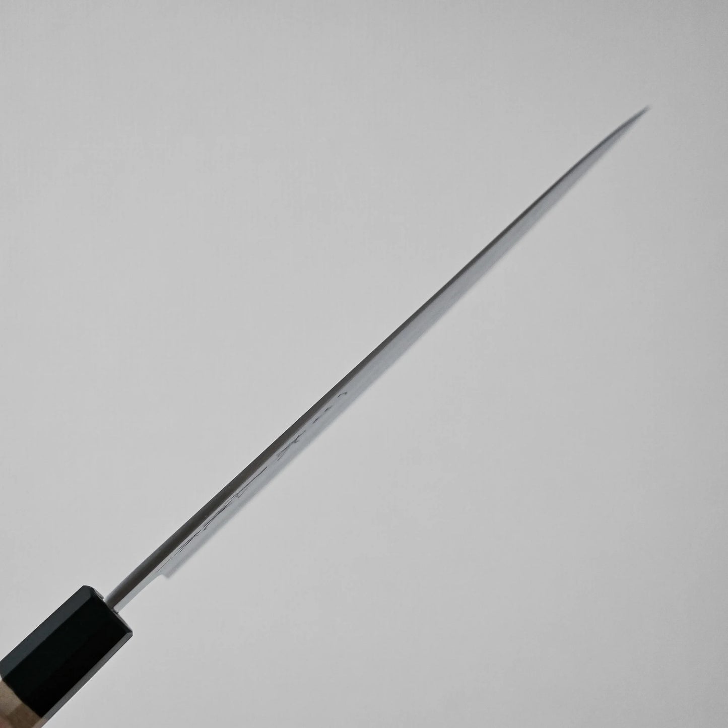 A close-up of kitchen knife shows its spine against a plain light gray background, emphasizing the narrow profile from a side view.
