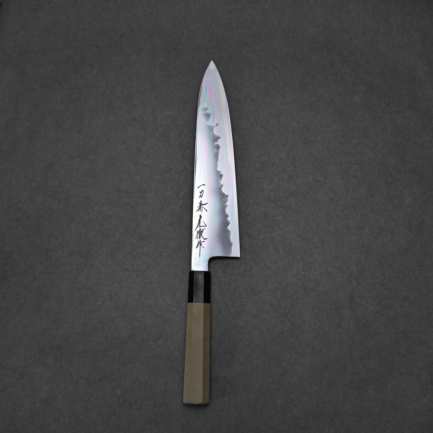 A Japanese chef’s knife with a wooden handle and patterned blade featuring Japanese characters, displayed on a dark gray textured background.