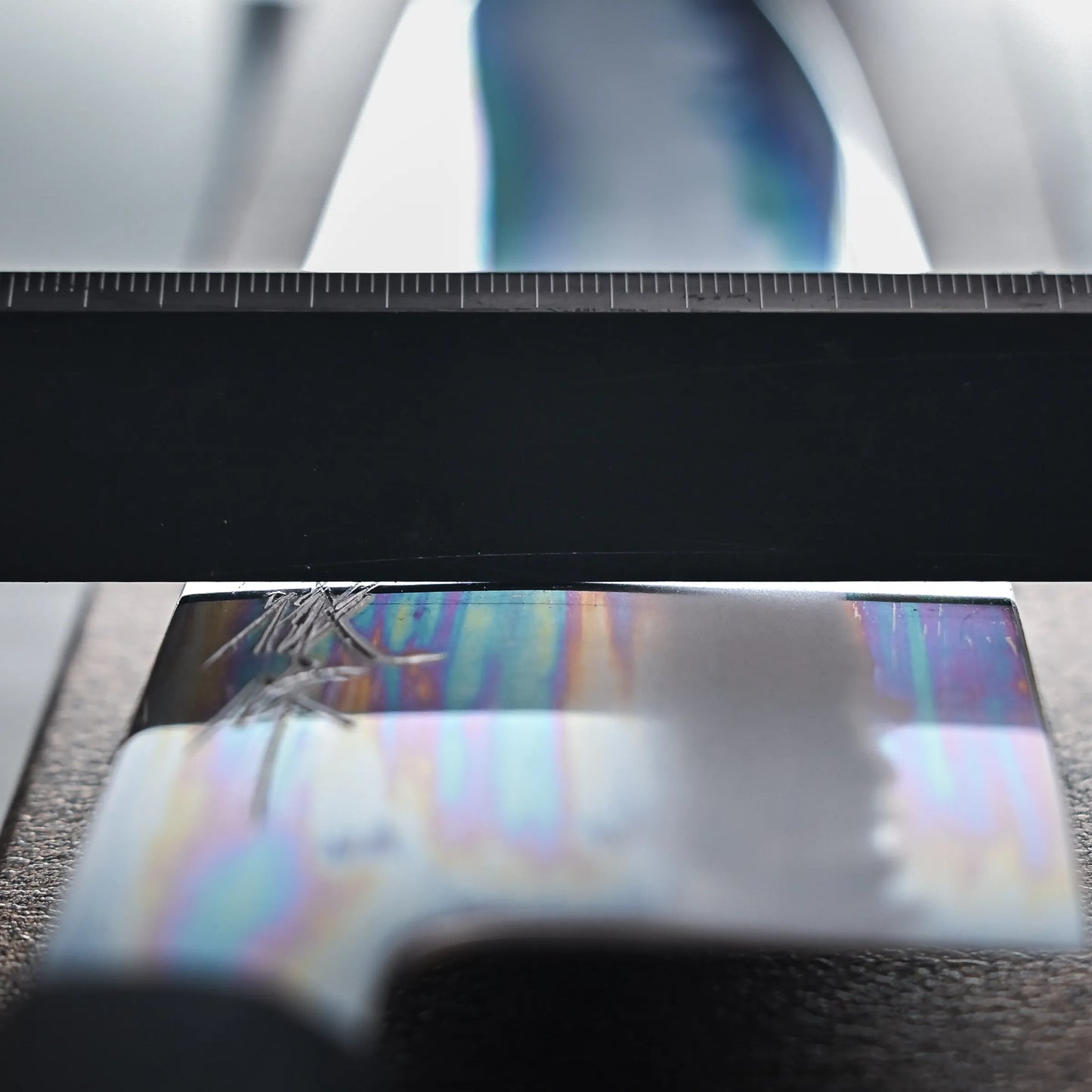 Close-up of the grind of the chef knife showing reflective surface with rainbow-like streaks beneath a ruler.