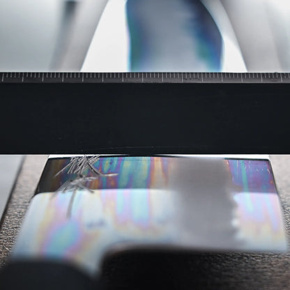 Close-up of the grind of the chef knife showing reflective surface with rainbow-like streaks beneath a ruler.