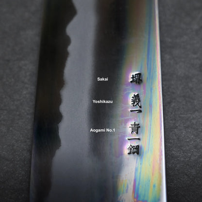 Close-up of a Japanese chef’s knife blade with an iridescent sheen, featuring English and Japanese inscriptions that read Sakai, Yoshikazu, and Aogami No. 1.