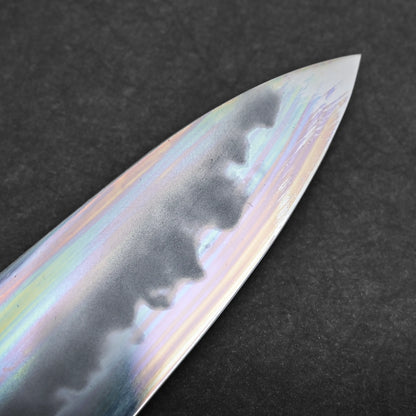 Close-up of a tall gyuto knife blade showing a wavy hamon pattern and an iridescent, rainbow-like finish, set against a dark, textured background.