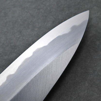 Close-up of a shiny Tanaka AS gyuto blade with a visible hamon pattern along the edge, set against a dark, textured background.