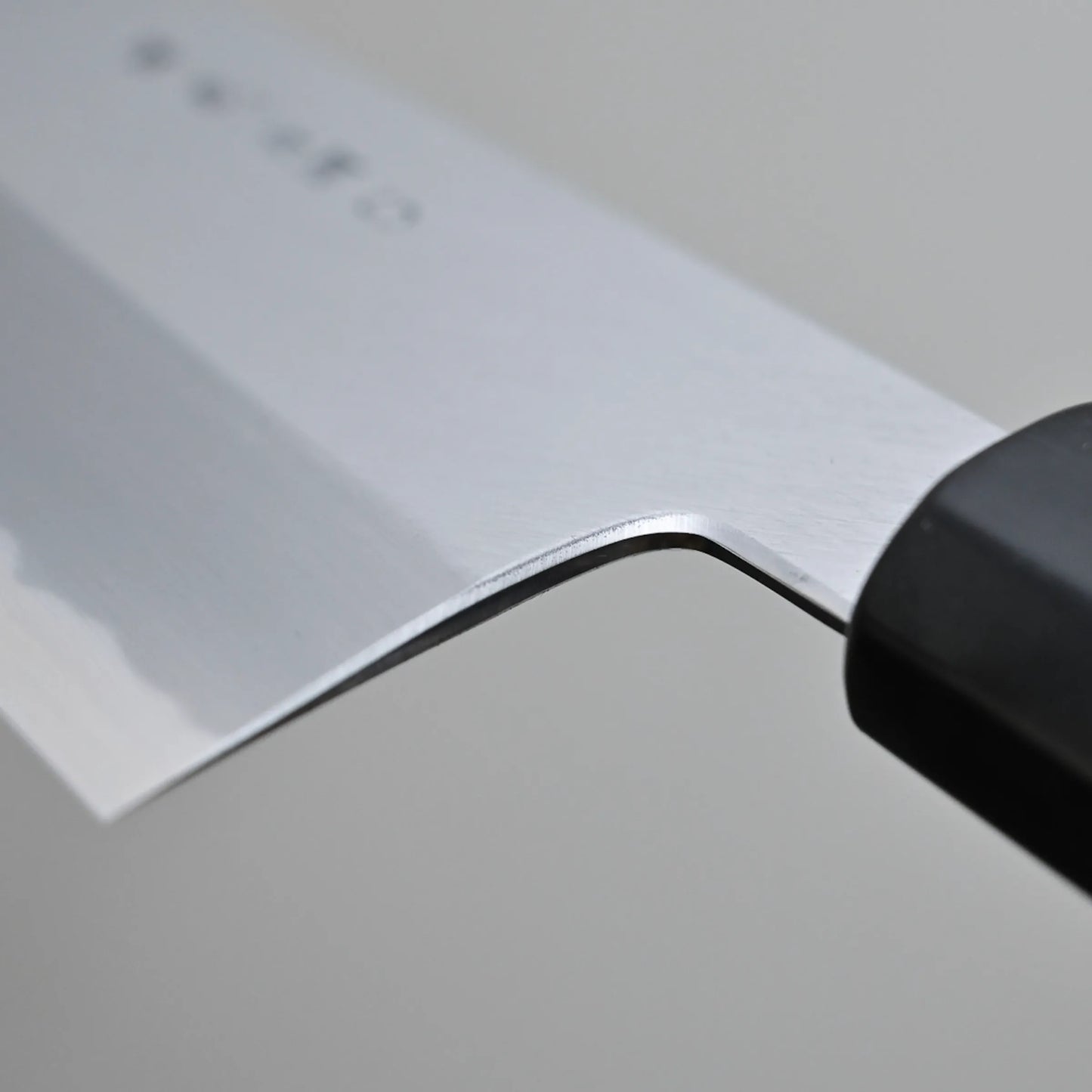 Close-up of choil finish of a Tanaka AS gyuto, set against a plain gray background.