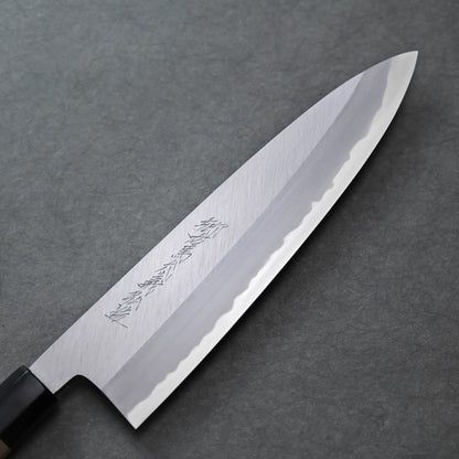 A Tanaka AS tall gyuto with a shiny blade and Kanji engravings rests on a gray textured surface. The blade features a wave-like pattern near the edge.