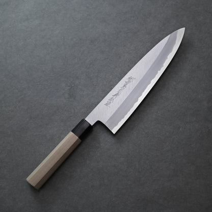 Yoshikazu Tanaka shinogi AS tall gyuto 240mm chef’s knife with a wooden handle and a silver blade featuring engraved characters, placed on a dark gray textured surface.