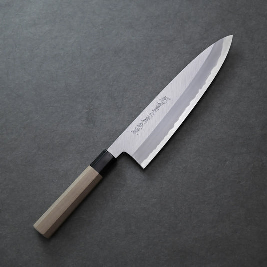 Yoshikazu Tanaka shinogi AS tall gyuto 240mm chef’s knife with a wooden handle and a silver blade featuring engraved characters, placed on a dark gray textured surface.