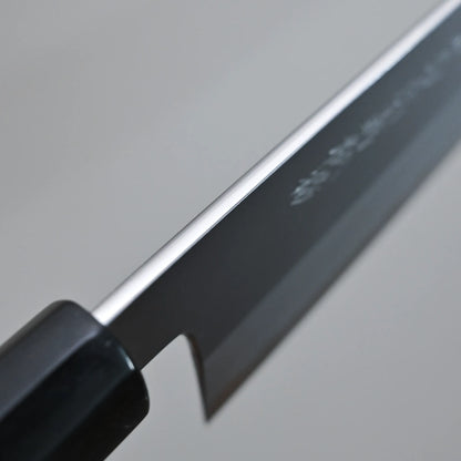 Close-up view of the spine of a Tanaka AS gyuto against a plain, blurred background.