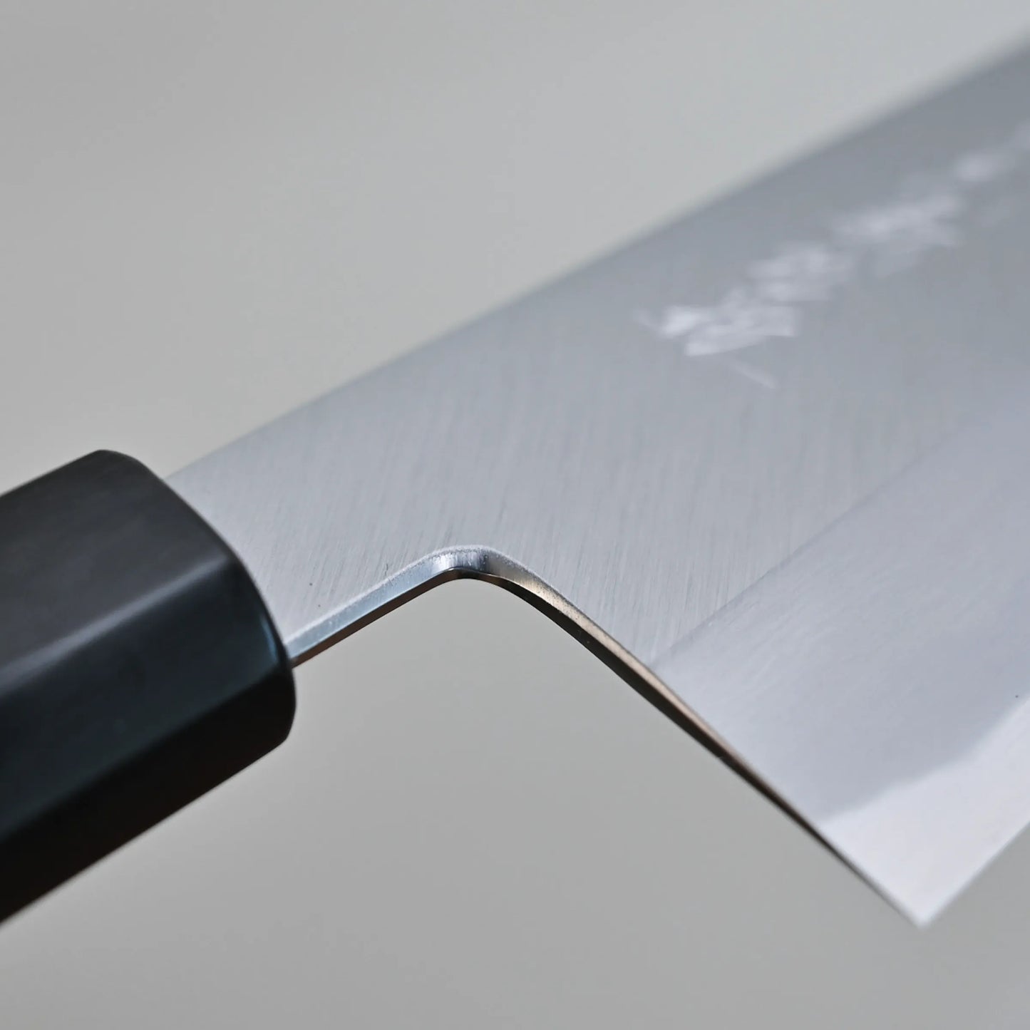 Close-up view of the choil finish highlighting the clean edge and part of the black handle against a plain background.