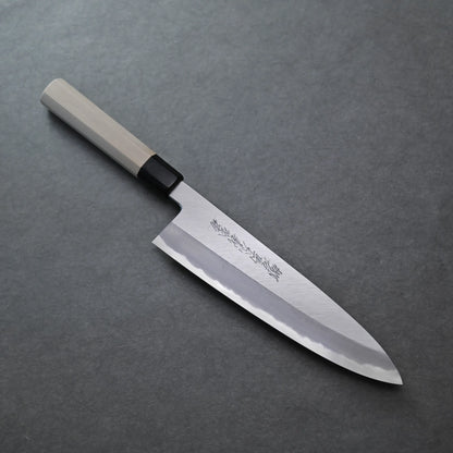 A Japanese chef’s knife with a light wood handle and an engraved blade rests diagonally on a dark gray textured surface, showcasing its elegant design.