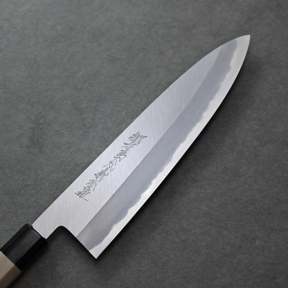 A close-up of a Japanese-style knife with a polished steel blade, visible hamon line, engraved characters, and a wooden handle resting on a dark grey textured surface.