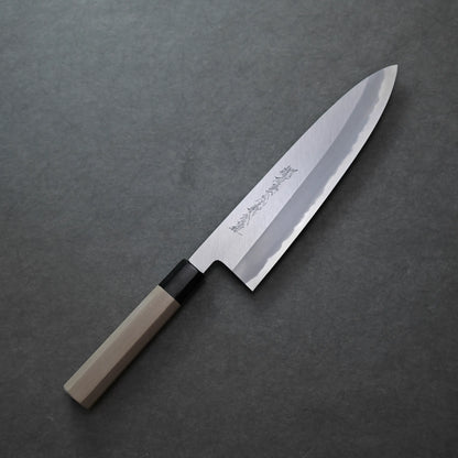 Yoshikazu Tanaka shinogi shirogami#1 tall gyuto 240mm with a wooden handle and a polished, engraved blade rests on a dark, textured surface, showcasing exquisite craftsmanship.