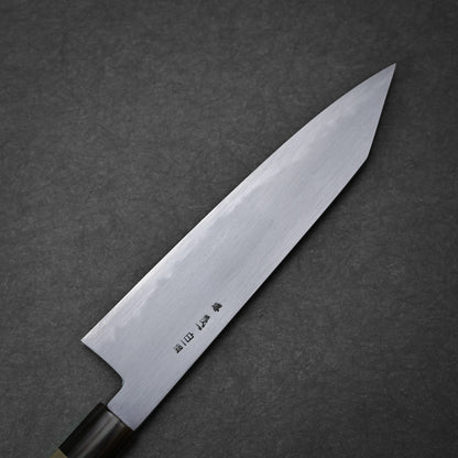 The Yoshikazu Tanaka shirogami#1 kiritsuke gyuto 225mm, featuring a pointed blade and Japanese characters near the handle, is crafted by Yoshikazu Tanaka and displayed on a dark textured surface.