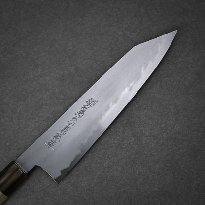 A close-up of the Yoshikazu Tanaka shirogami#1 kiritsuke gyuto 225mm, a Japanese chefs knife with engraved kanji on the blade and a wooden handle, crafted in Sakai by Yoshikazu Tanaka. The knife rests on a dark textured surface.