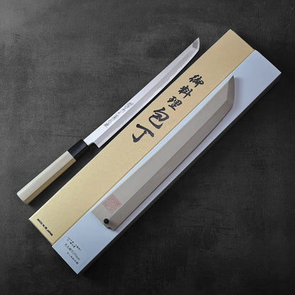 A sakimaru sujihiki with saya rests beside its box, showcasing refined lines and a harmonious silhouette.