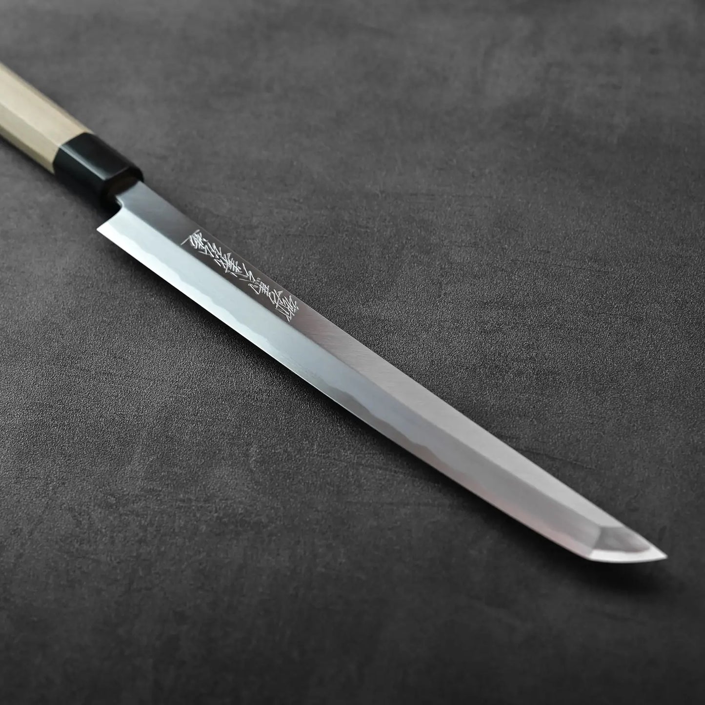 A sakimaru sujihiki 270mm with a saya is displayed, highlighting its long, slender blade and wooden cover.