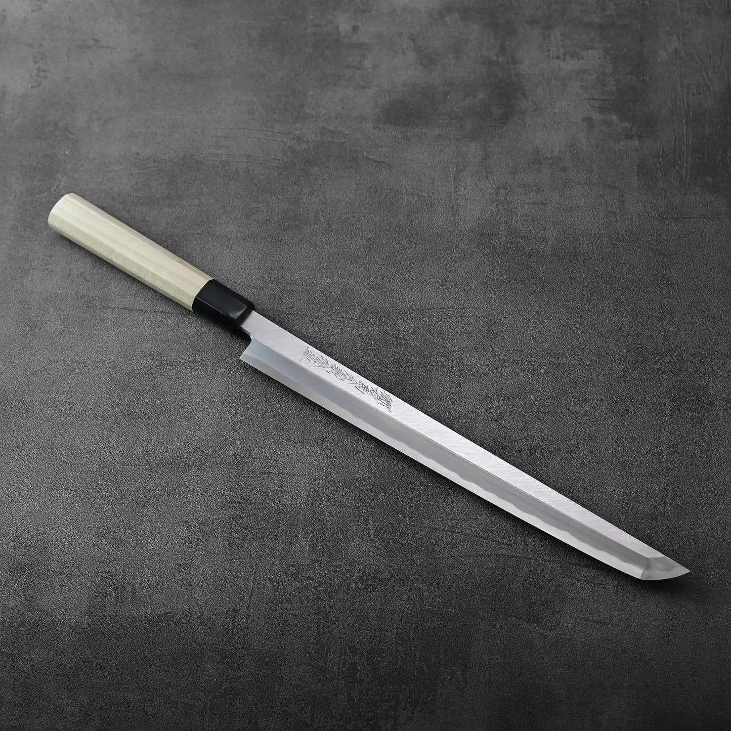 Sakimaru sujihiki 300mm (with saya) resting, blade exposed and polished finish with wooden sheath alongside.