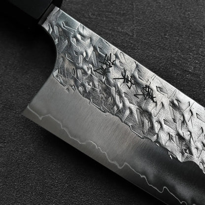 Gyuto with a textured blade and engraved kanji, shown in close-up to highlight its detailed finish.