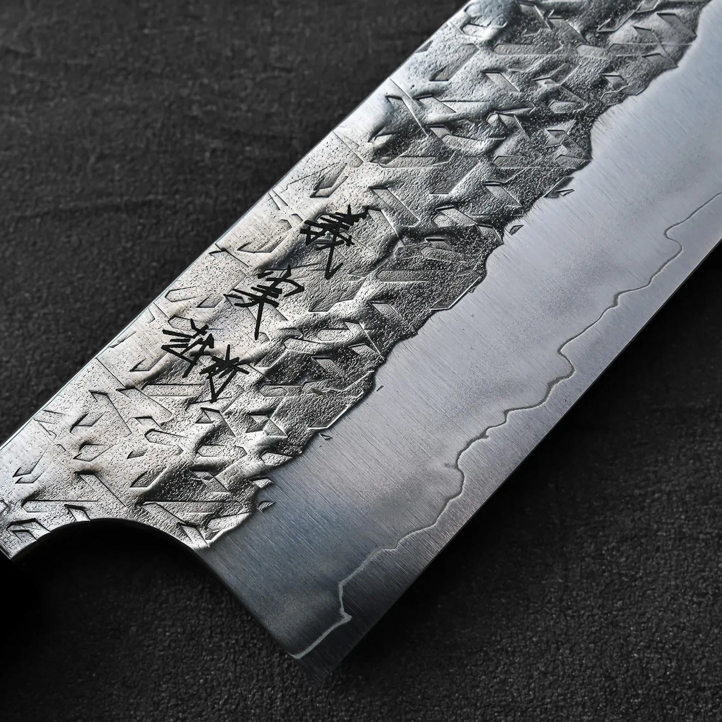 Close-up of a gyuto blade showing kanji engraving, highlighting steel texture and engraved details.