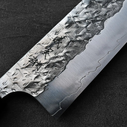 Close-up of a gyuto blade showing kanji engraving, highlighting steel texture and engraved details.