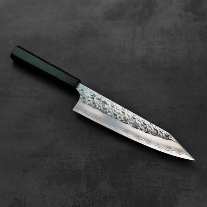A kiritsuke gyuto with a dark handle and textured blade is displayed, highlighting its features.