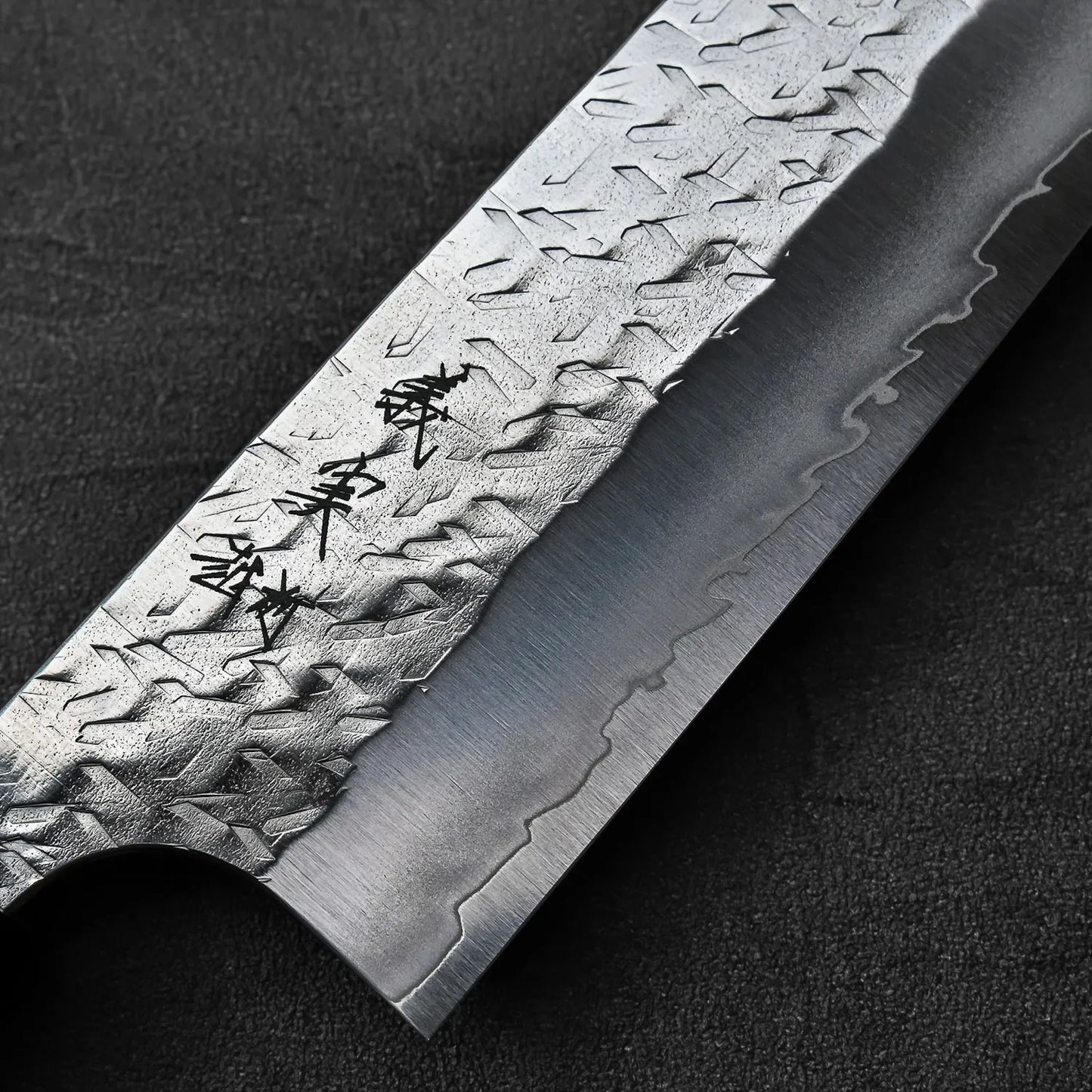 Close-up of kiritsuke gyuto blade featuring hammer marks and Kanji on the metal.