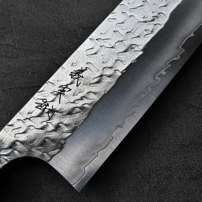 Close-up of kiritsuke gyuto blade featuring hammer marks and Kanji on the metal.