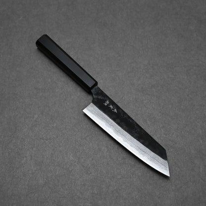 A Yoshimi Kato kurouchi damascus AS bunka 170mm knife with a dark handle and wide patterned blade rests on a flat, dark gray surface. Subtle markings are visible near the handle on its Aogami Super steel blade.