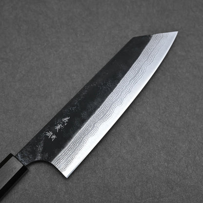 A Yoshimi Kato kurouchi damascus AS bunka 170mm knife with a dark handle and patterned blade, showing wavy layers and engraved characters, rests on a dark gray textured surface.