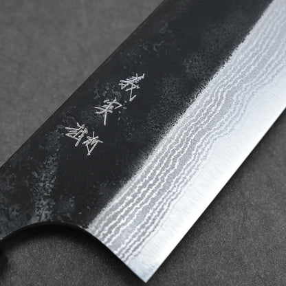 Close-up of the Yoshimi Kato kurouchi damascus AS bunka 170mm blade, featuring wavy damascus patterns and engraved Japanese characters on the dark upper section. Made from Aogami Super steel for outstanding performance against a textured background.
