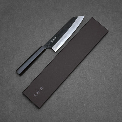 The Yoshimi Kato kurouchi damascus AS bunka 170mm, featuring a black handle and patterned blade, rests beside a dark knife box with white text, all displayed on a textured gray surface.