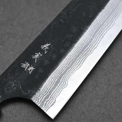 Close-up of a Yoshimi Kato kurouchi damascus AS kiritsuke gyuto 210mm blade, highlighting wavy Damascus layers and kanji engraving on a dark surface.