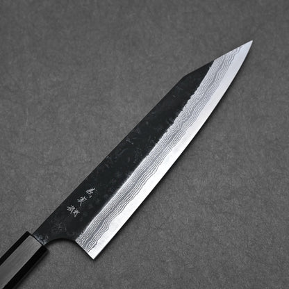 The Yoshimi Kato kurouchi damascus AS kiritsuke gyuto 210mm features a dark handle, Aogami Super blade with wavy damascus patterns, and Japanese characters on the metal, displayed on a textured gray surface.