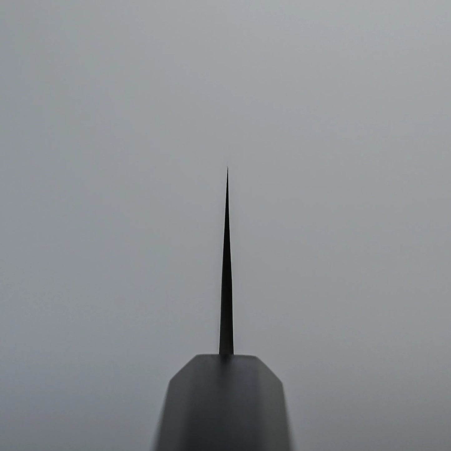 Choil shot of a Kato santoku knife blade photographed from the handle, with the blade pointing upward against a plain gray background.