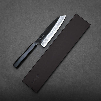 A Kato santoku knife with a dark handle and a patterned steel blade rests beside a closed, rectangular black box on a dark grey surface.