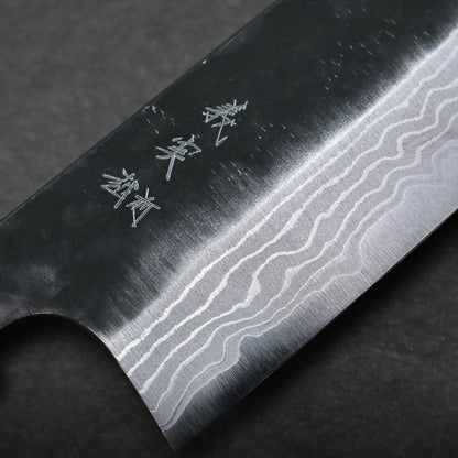 Close-up of a kurouchi damascus santoku blade reveals intricate wave-like Damascus steel patterns and Japanese characters engraved near the spine, set against a dark background.